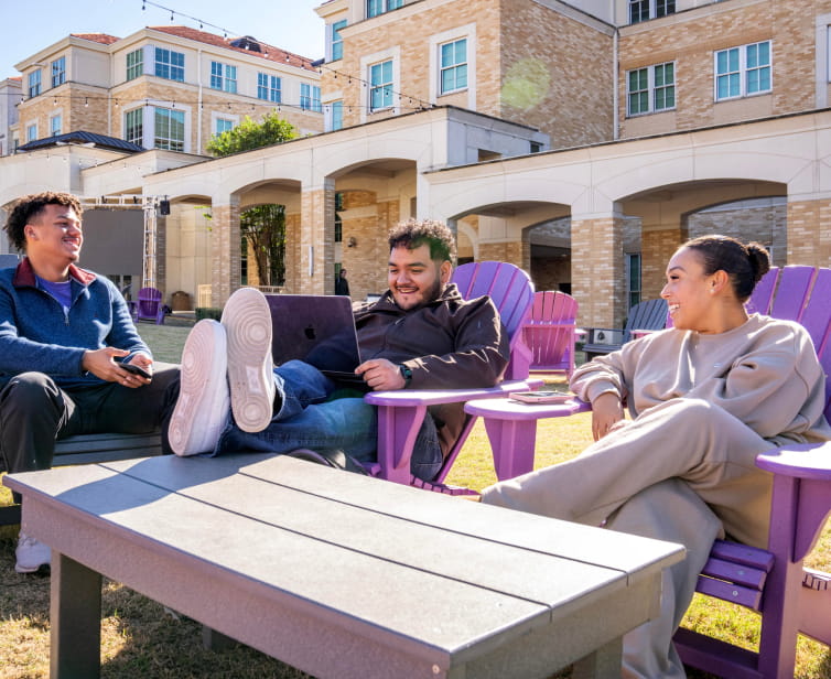Three students sit in purple lounge chairs in the Campus Commons lawn area