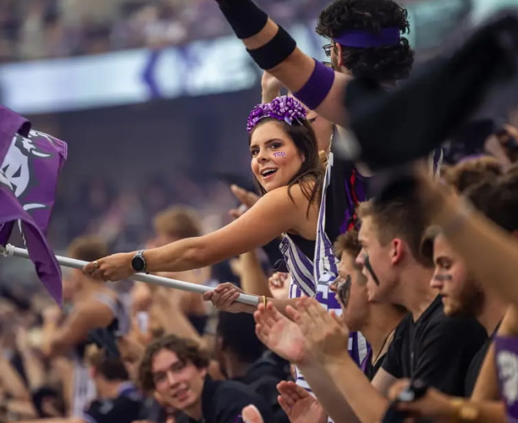 Female student waves a Horned Frog flag in a big group of TCU students while watching a football game
